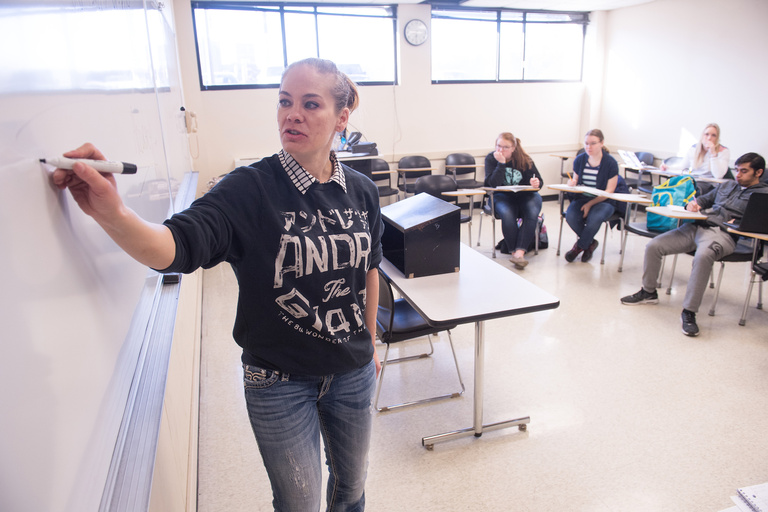 A woman writing on a whiteboard in front of a class