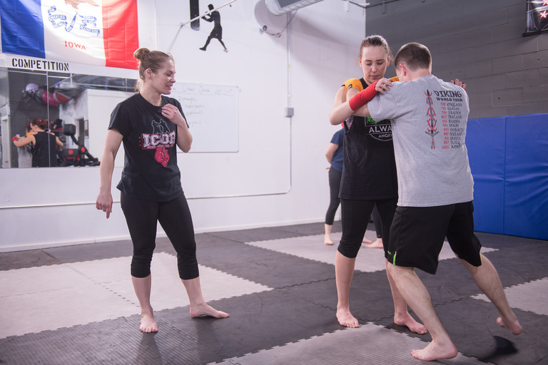 A woman giving instruction to two people grappling with each other