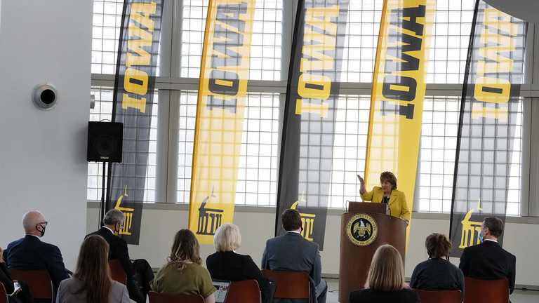 the new University of Iowa president addresses the media; Iowa banners fly in the background