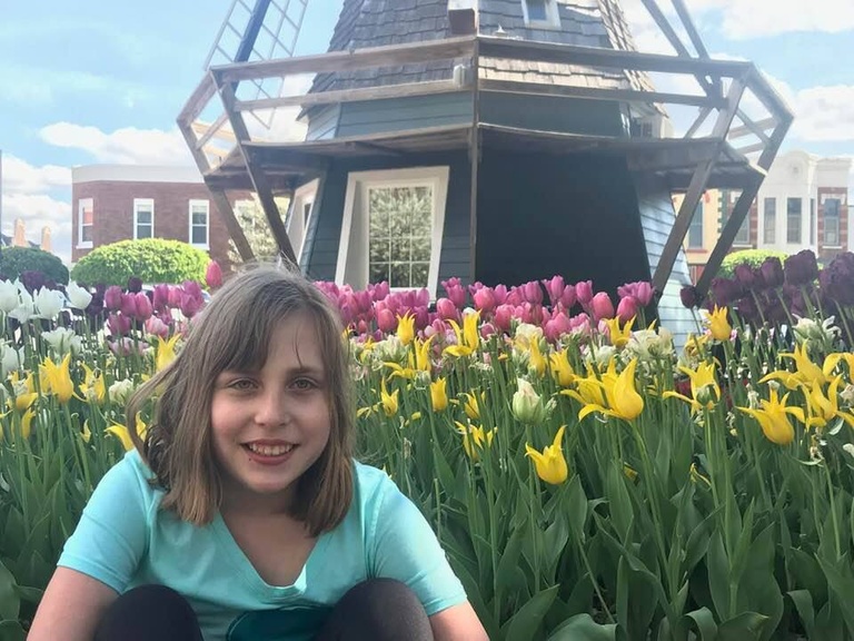 a girl sitting in front of a bed of flowers