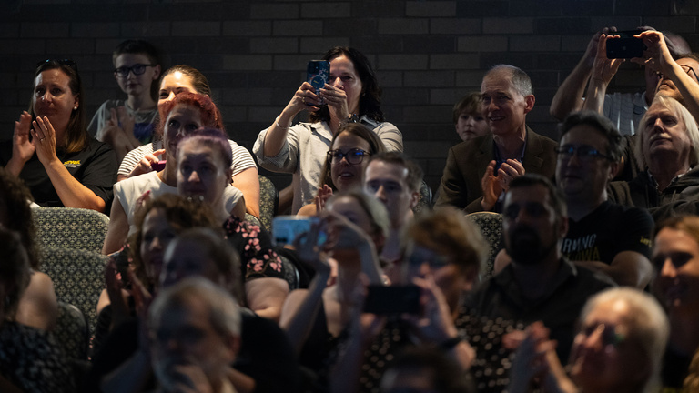 people in auditorium seats applauding and capturing visuals with their phones