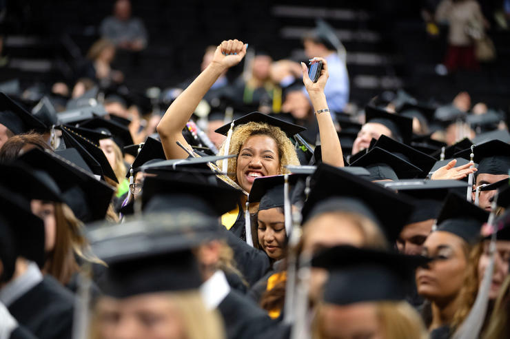University of Iowa students gather at commencement; one student can be seen raising her arms in celebration