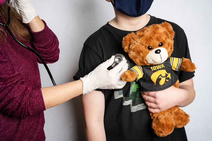 A child is examined while holding a teddy bear