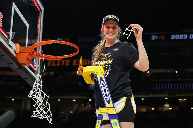 University of Iowa women's basketball player Sharon Goodman standing on a ladder holding a strand of netting after a basketball game