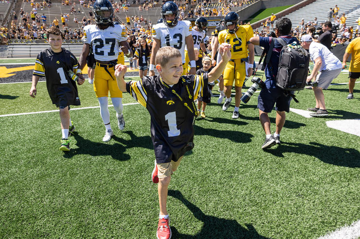 Kid Captain Wyatt Rannals walks on a football field with both arms raised