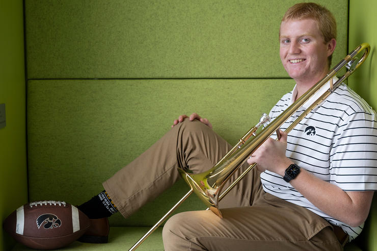 University of Iowa graduate Carter Shockey holding a brass instrument while sitting near a football