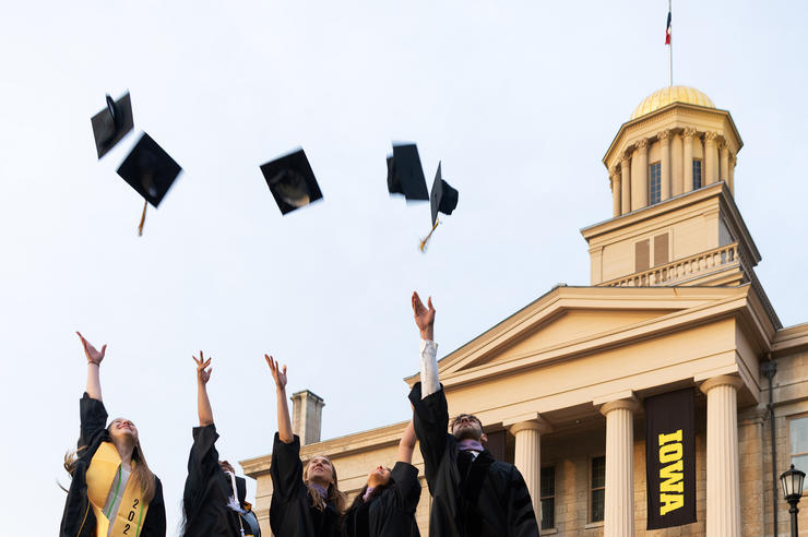 graduates throwing caps in the air near Old Capitol on the University of Iowa campus