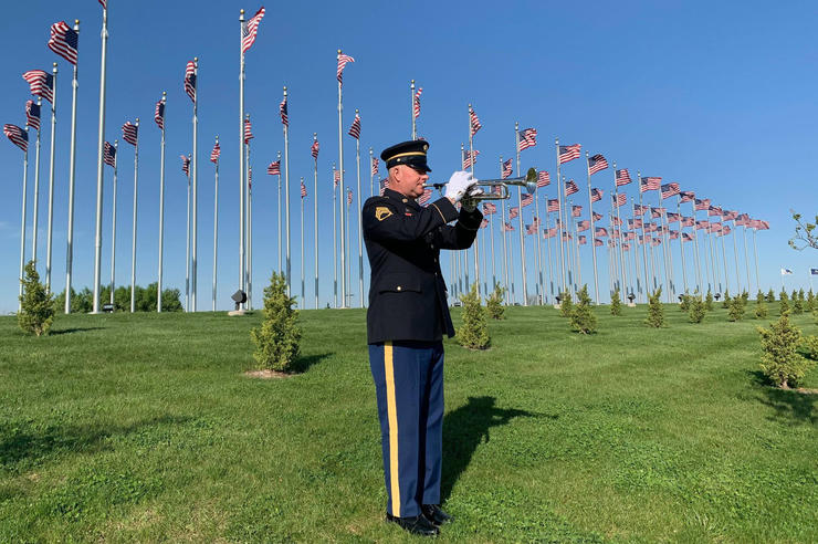 Jeff Six playing the trumpet outdoors, in front of numerous flag poles with US flags flying
