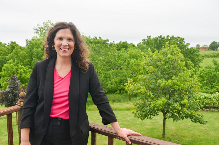 a woman standing on a deck with a green, wooded area in the background