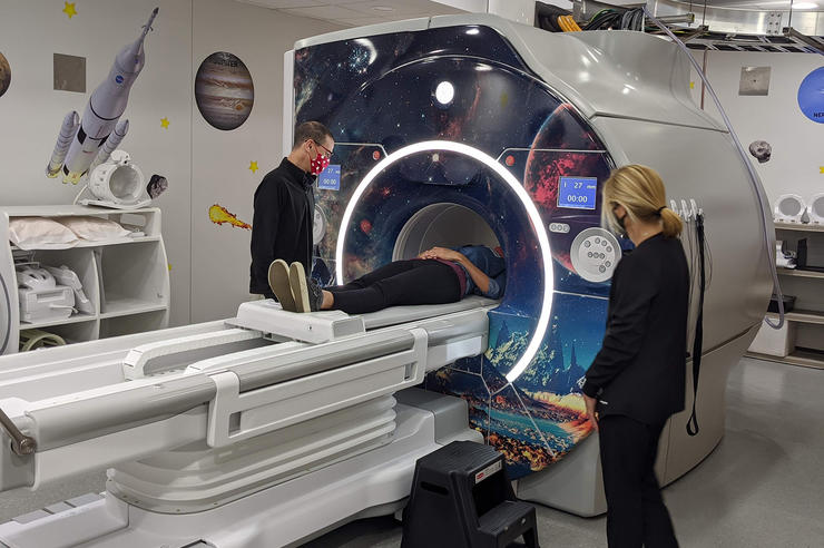 two people standing near an MRI machine with space visuals applied to it; a third person is the opening of the machine