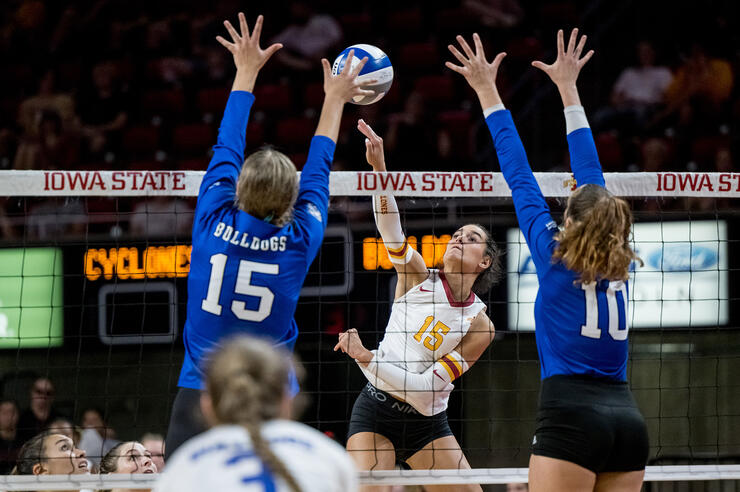 Iowa State University volleyball player Kiersten Schmitt rises up to hit the ball as two opponents attempt to block the shot