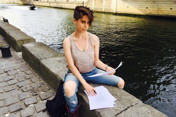 University of Iowa alumna Jen Silverman sit on the banks of a river with papers in hand and in front of her