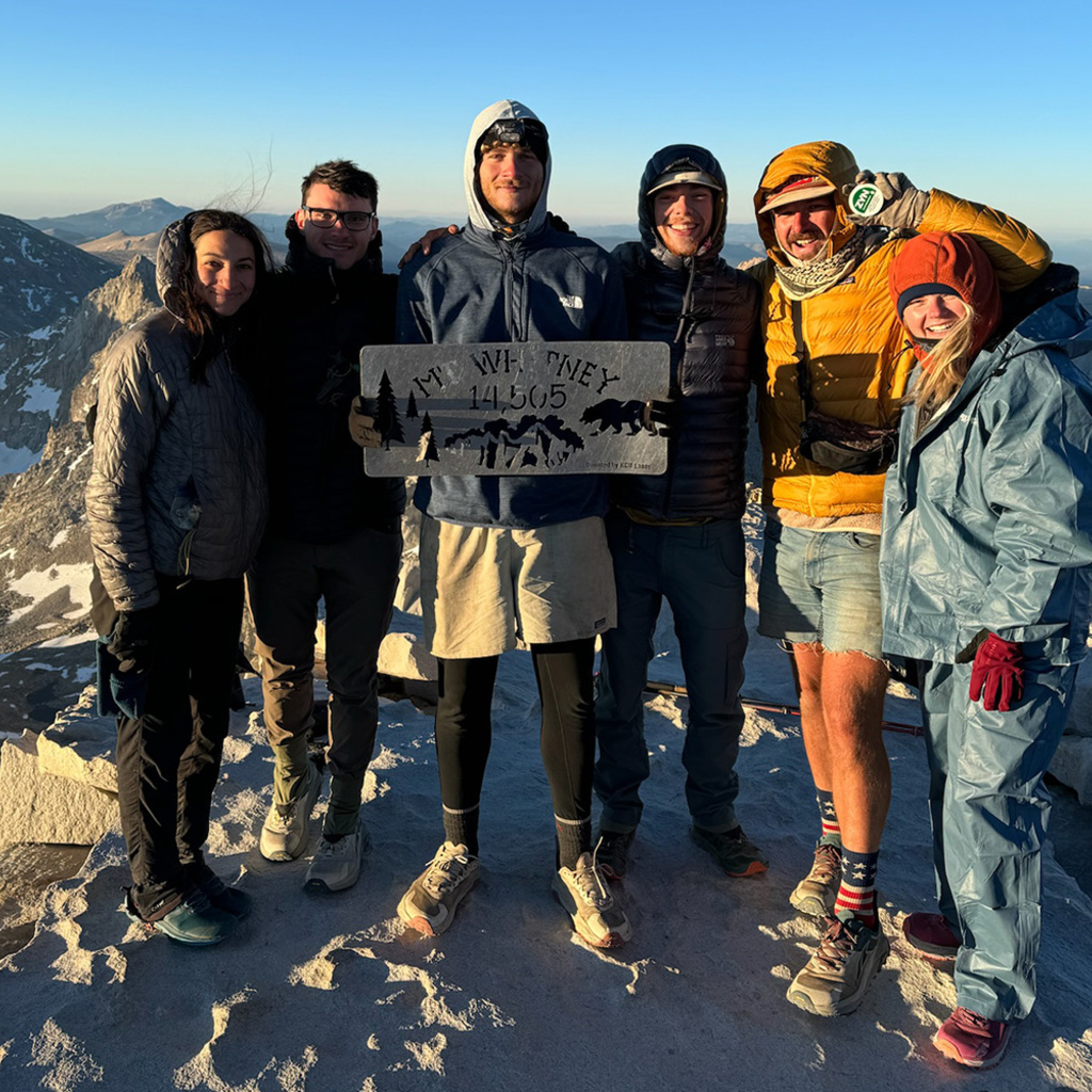 a group of people next to a sign atop Mount Whitney