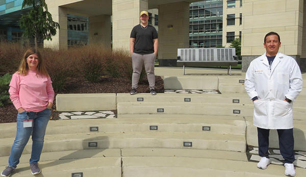 Three University of Iowa employees who were temporarily reassigned to work at the State Hygienic Laboratory stand outdoors, following social distancing guidelines