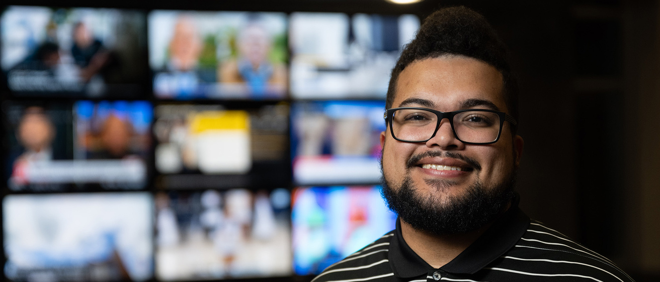 A man standing in front of multiple screens posing for a portrait