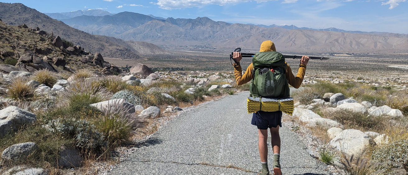 a man walking on a path with mountains visible in the distance