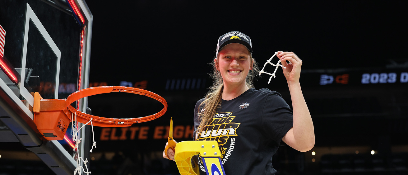 A basketball player holding up a piece of the net she just cut down and smiling