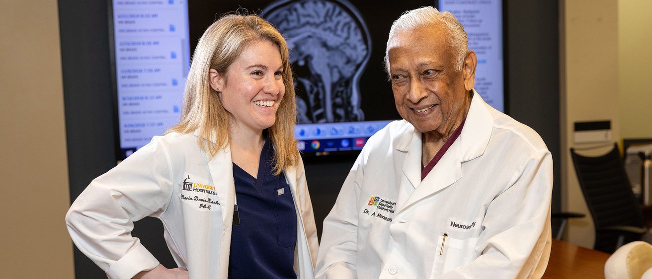 Two doctors smiling for a photo in front of a screen