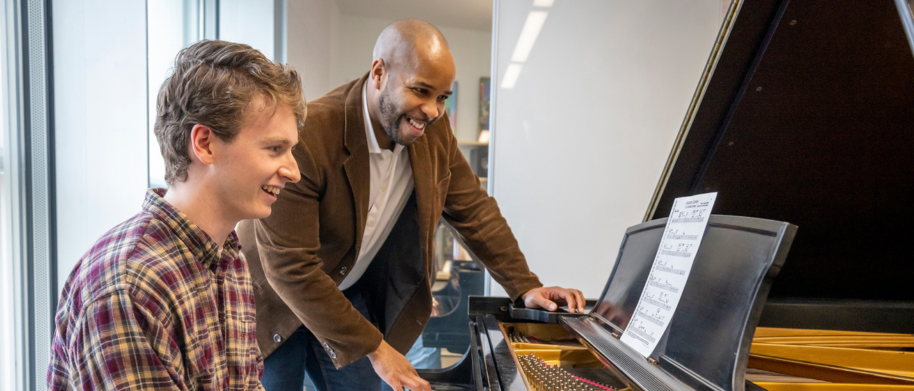 two men sitting behind a piano testing a song