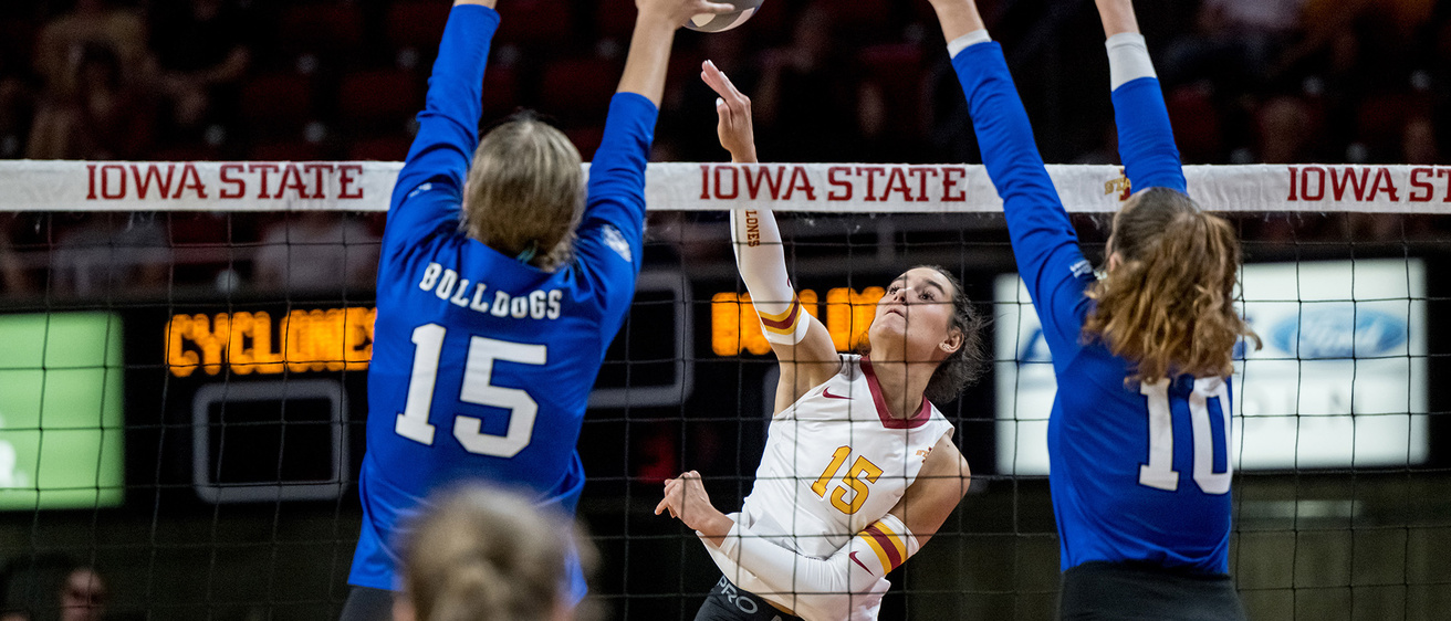 a volleyball player leaps to spike the ball while two defenders jump in an attempt to block