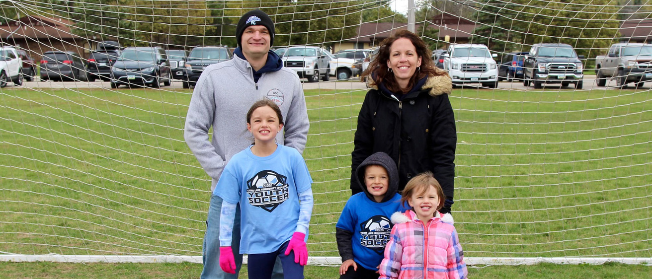 A family of five standing in font of a soccer net