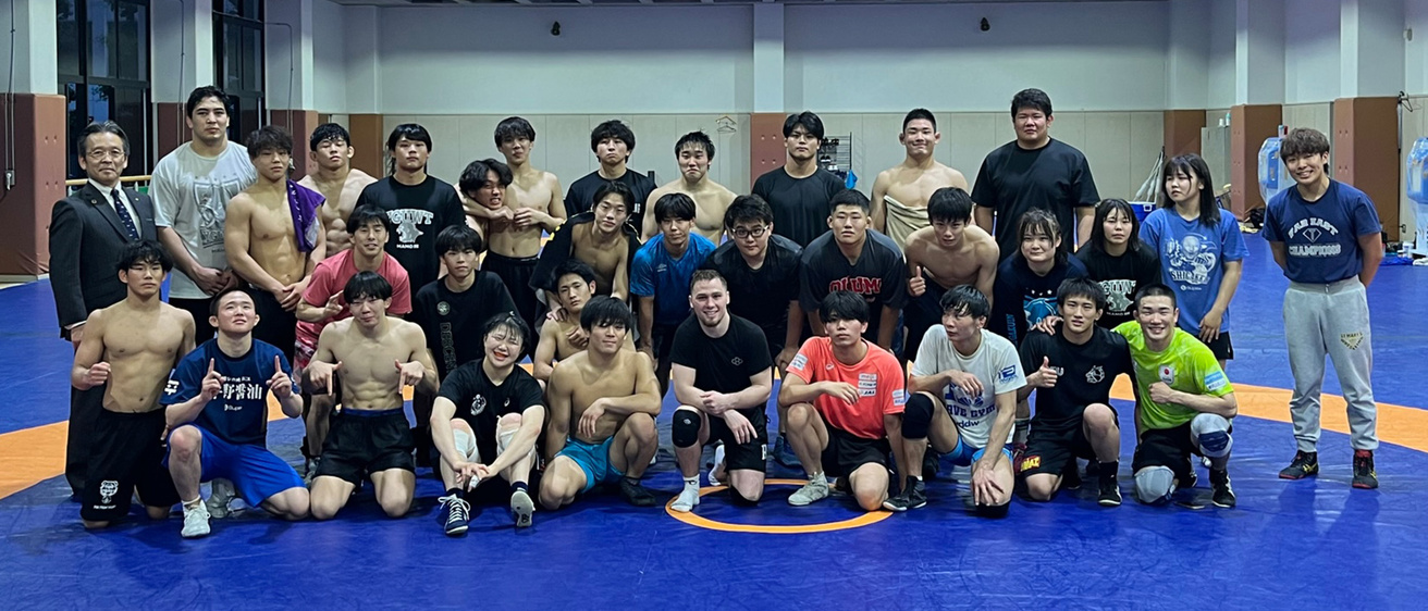 A group of wrestlers standing on a mat smiling