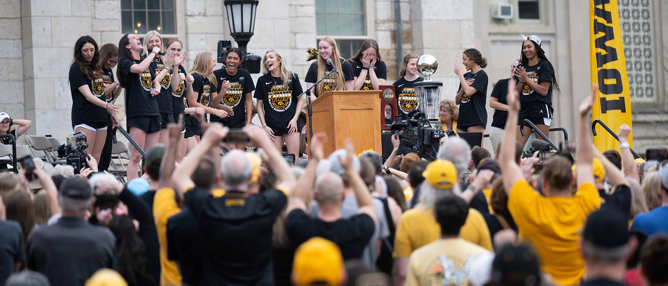 A group of peple on stage with a cheering crowd below them
