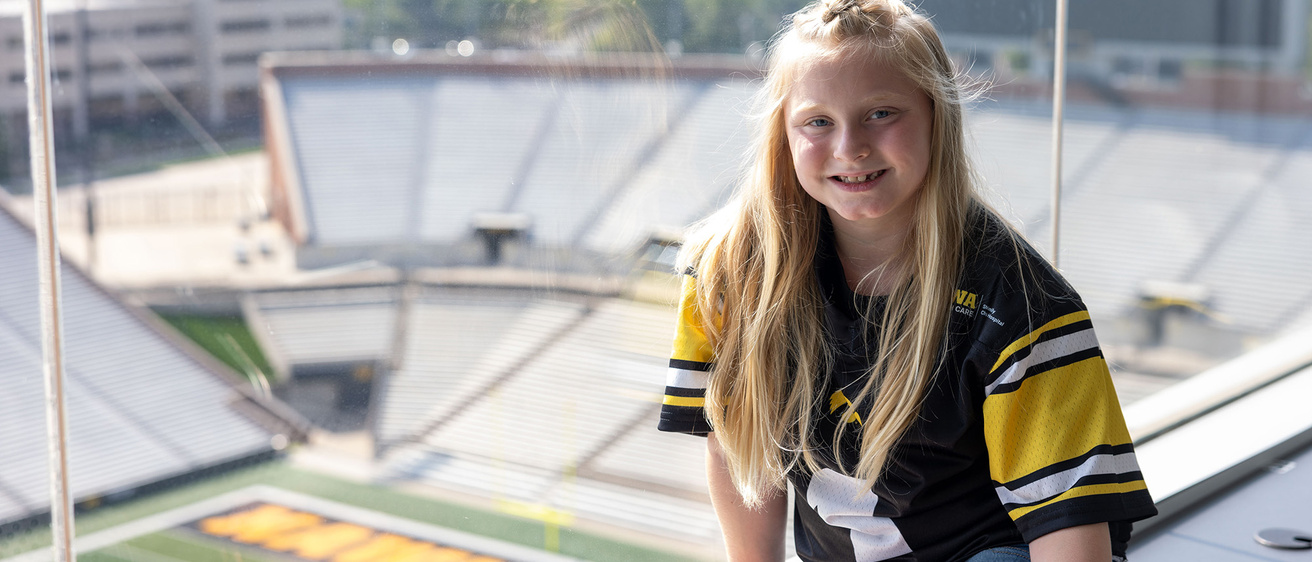 A young girl sitting on a window sill looking over a football field