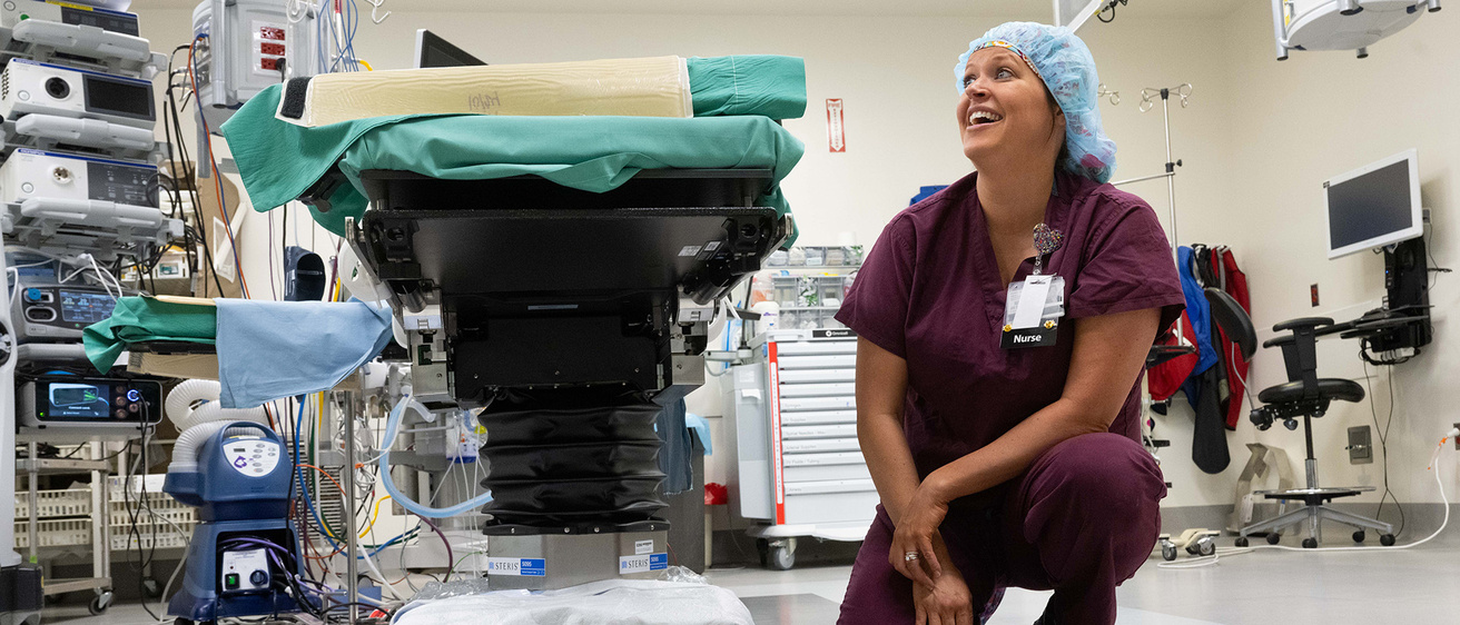 a nurse crouches down next to a hospital bed with a protective product around its base