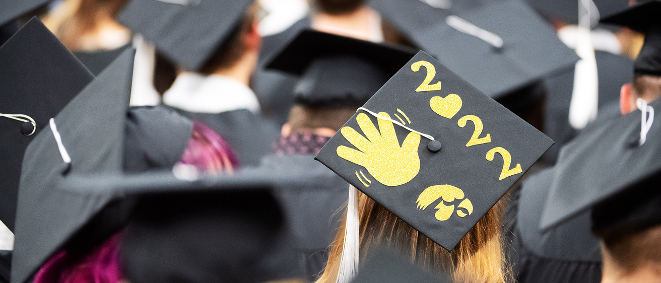 a scene from graduation, where one grad's cap features a waving hand and the year 2022 on it