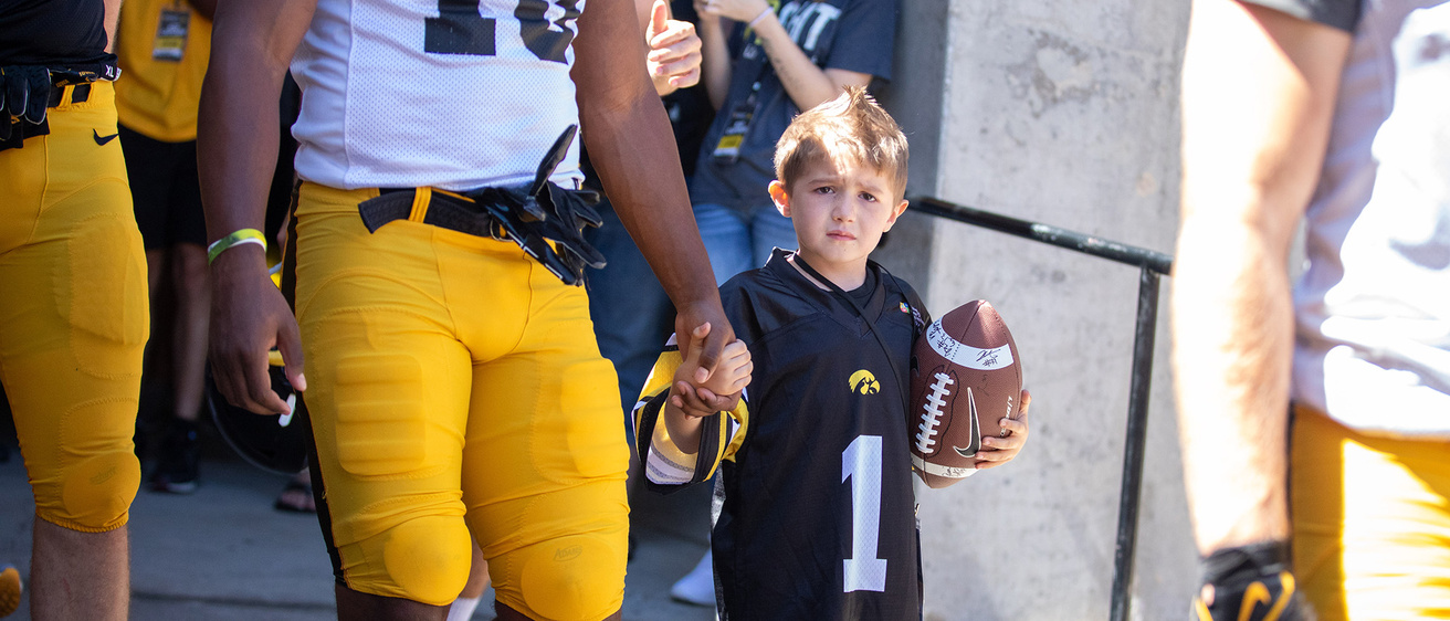 a young boy walking with a football player while holding a football