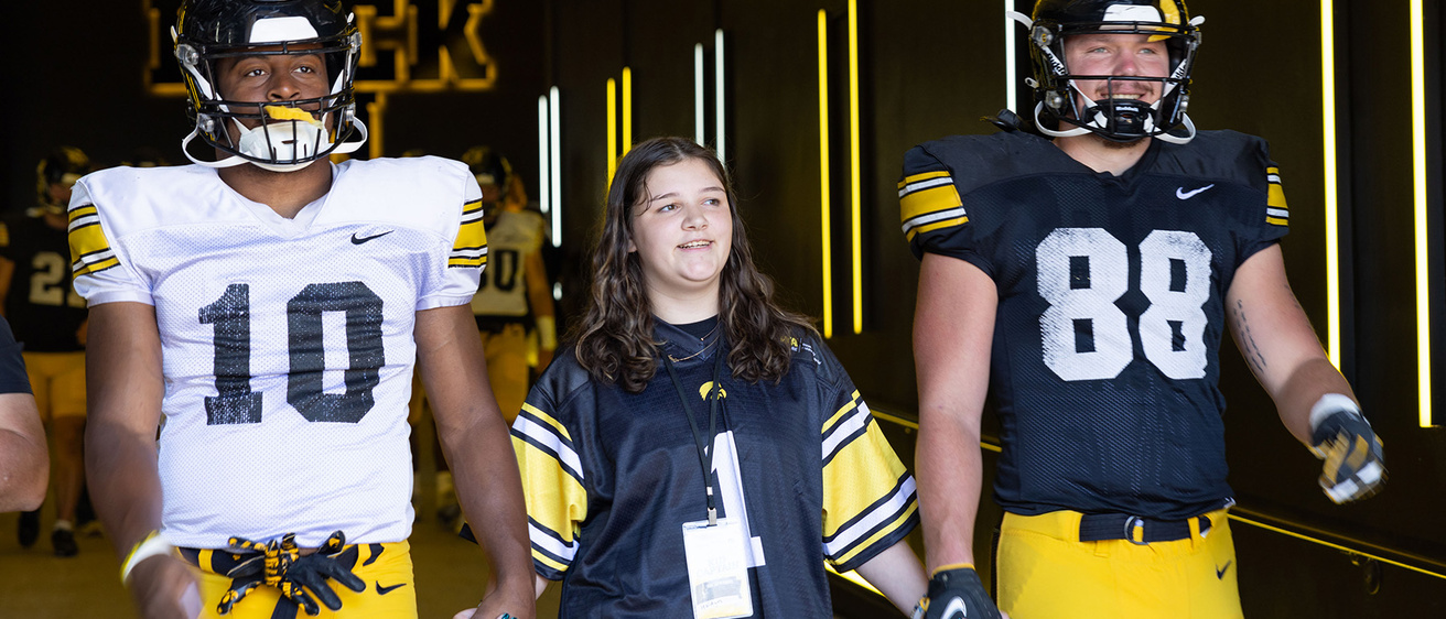 A girl standing with two football players walking through a tunnel