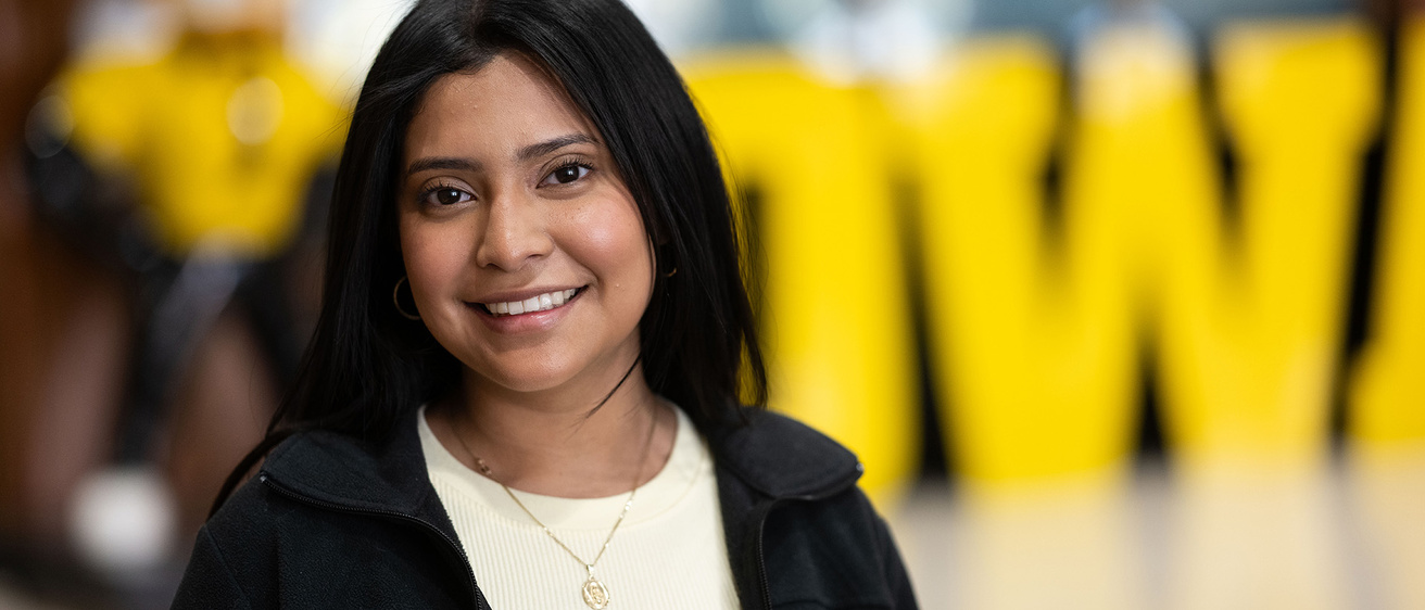 University of Iowa grad Brenda Ramirez with a Herky statue and an Iowa sign out of focus in the background