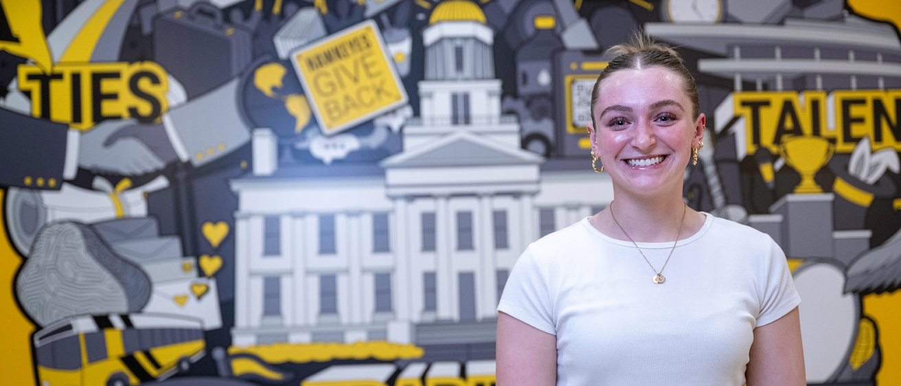 University of Iowa student Lillian Wischmeyer standing in front of an Iowa mural