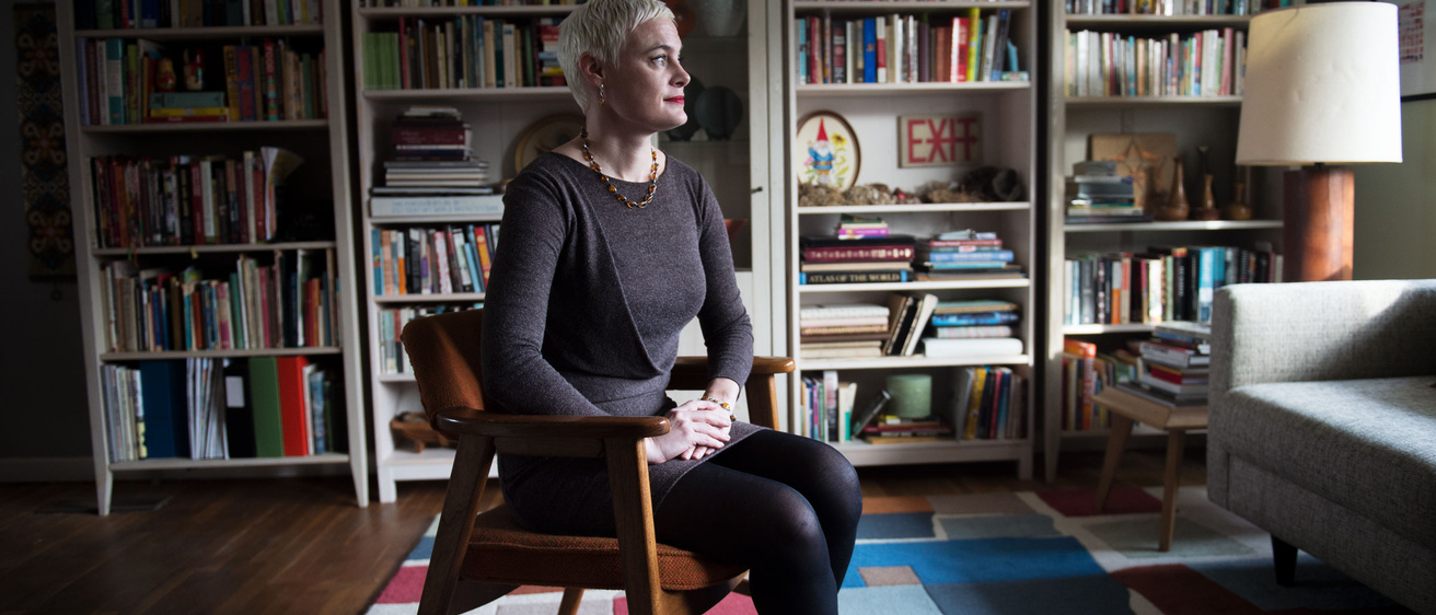 A woman sitting in a room with a wall lined with books