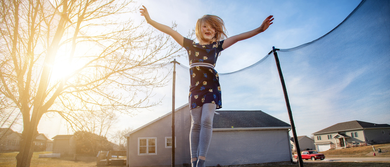 a young girl jumping on a trampoline outdoors in her neighborhood