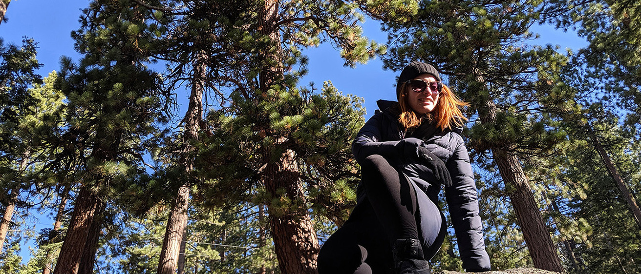 a woman atop a boulder in a wooded area
