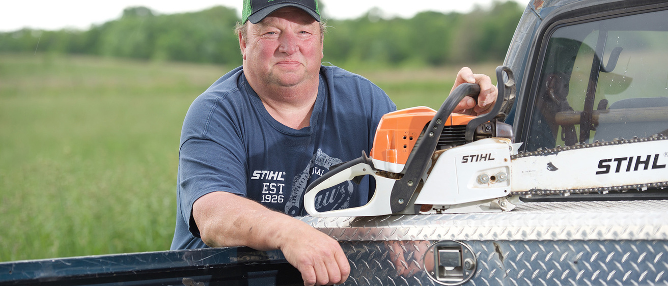 a man holding a chain saw by his truck