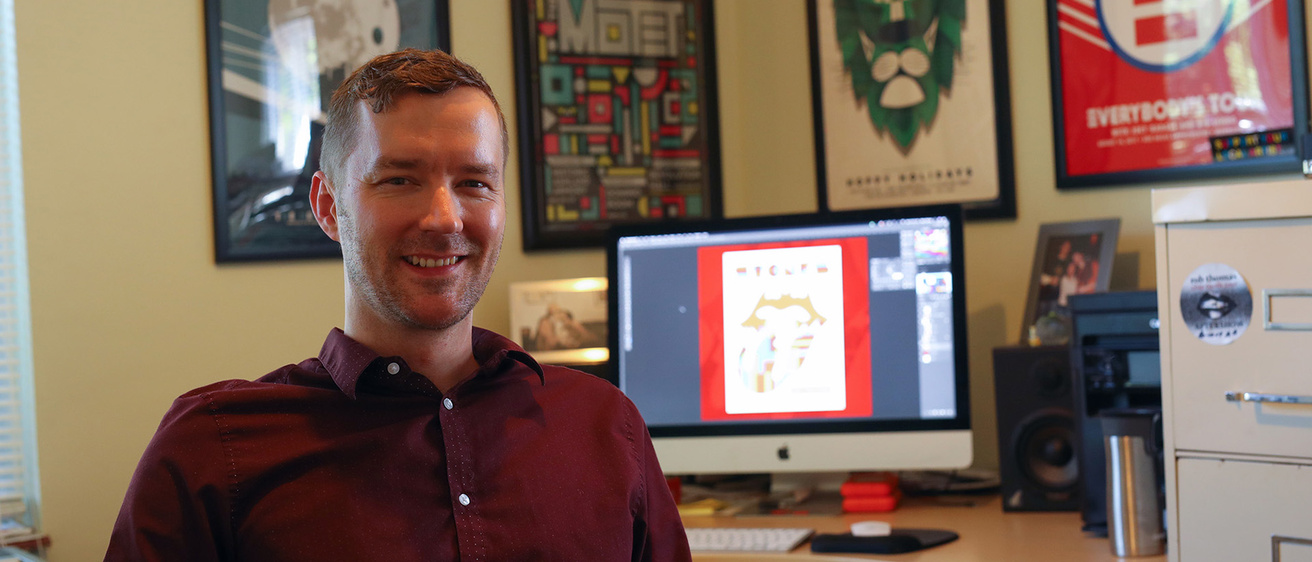 a man sitting in his office, the walls of which are adorned with posters he designed