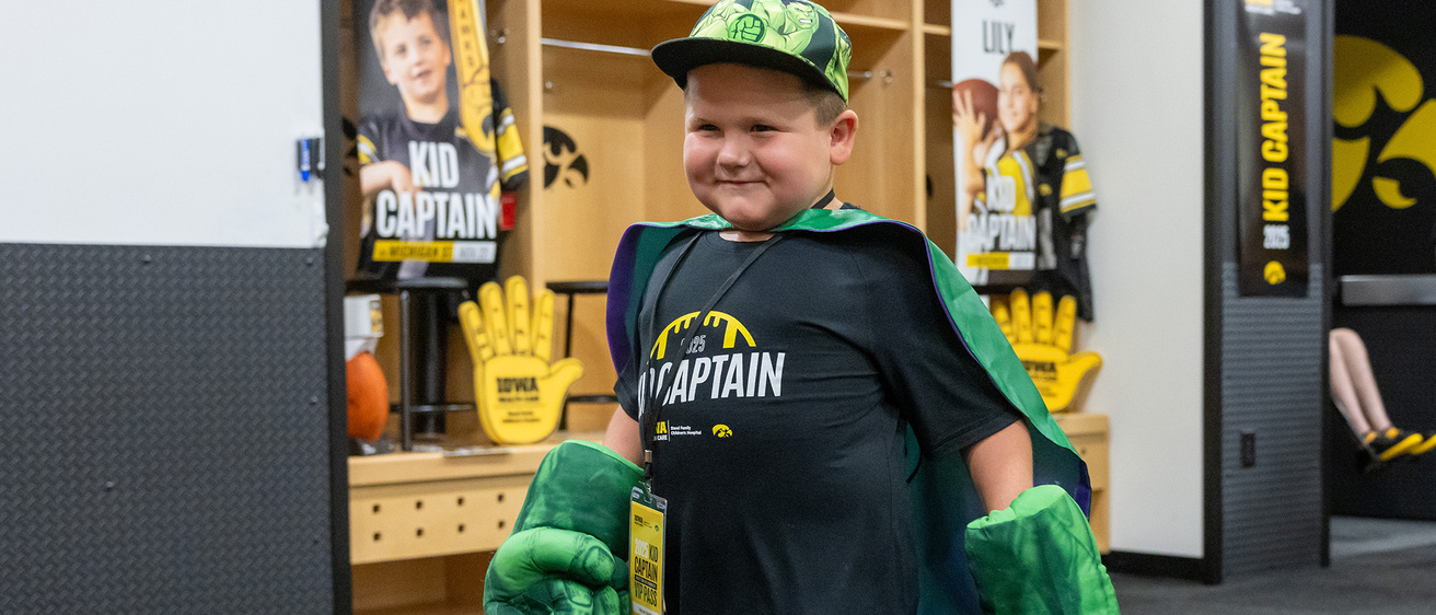 Kid Captain Micah Norby walking through the Kinnick locker room wearing Hulk hands and a cape