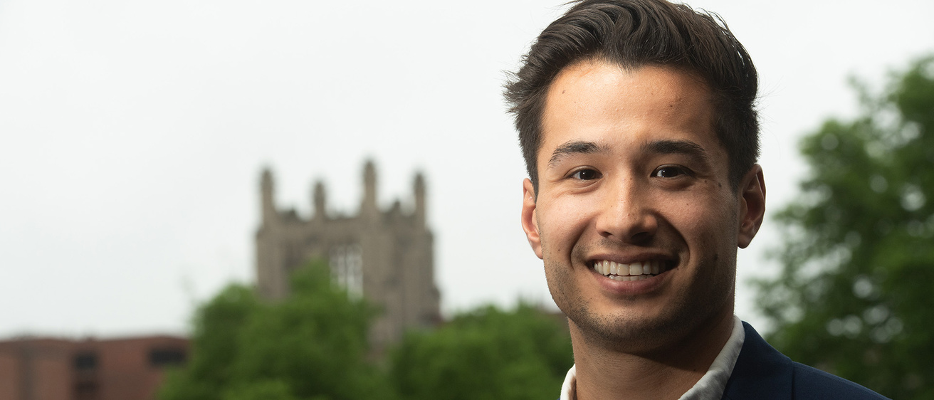 a man standing on the university of iowa campus with a gothic structure visible in the background