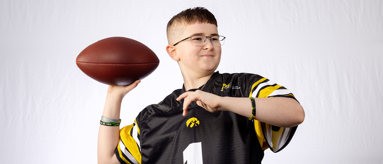 a young boy wearing an Iowa Hawkeyes jersey brings his arm back to throw a football