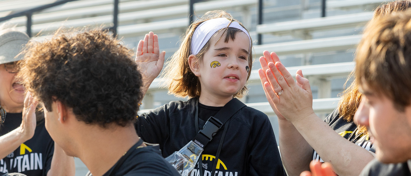 a young girl wearing an iowa hawkeyes jersey raises her hand to deliver a high-five to a nearby friend or family member