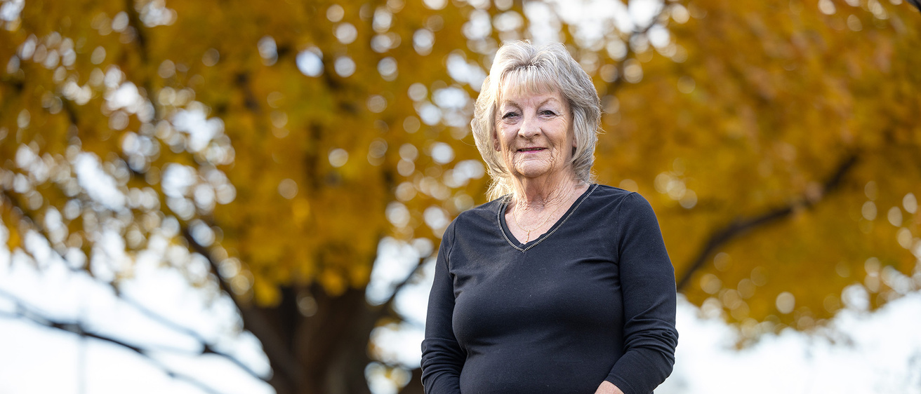 a woman posing outdoors near a tree with golden leaves