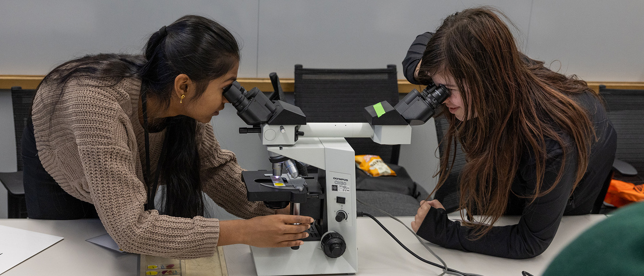 two middle school students look through a microscope at a Kids Go STEM event
