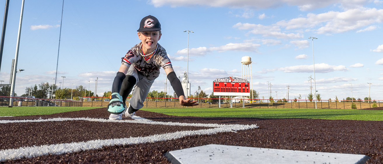 a boy sliding headfirst at home plate on a baseball field