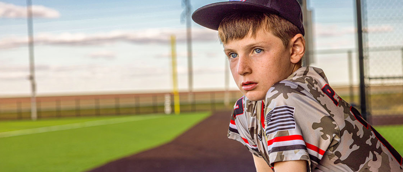 a young boy standing in a baseball dugout looks out toward the infield