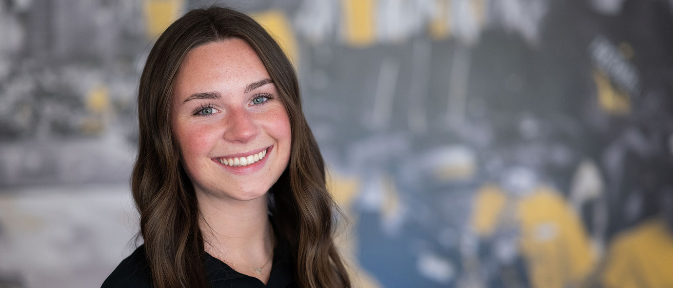 University of Iowa student Amelia Early stands in front of a black-and-gold themed wall that is in soft focus
