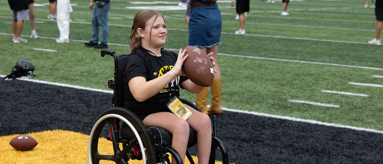Kid Captain Lily Lee in the end zone holding a football during Kids Day at Kinnick