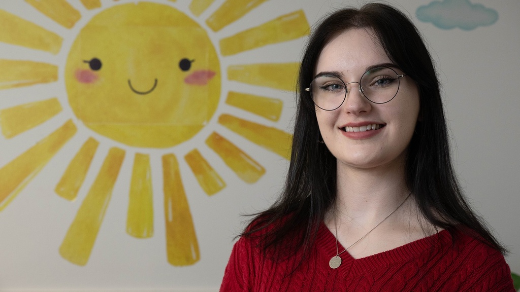 A woman standing in front of a mural of the sun smiling